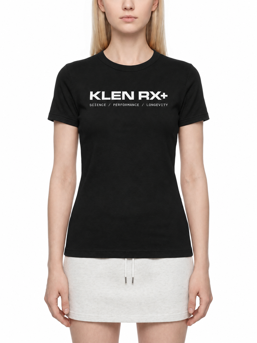 A woman wearing a fitted black short-sleeve T-shirt with white 'KLEN RX+' text across the chest, paired with a light gray mini skirt, against a plain white studio background.