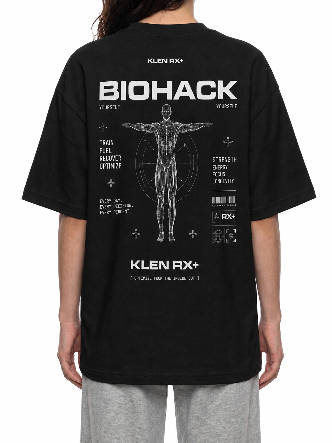 A person wearing a black oversized T-shirt from the back, featuring a large white sci-fi graphic with the text 'BIOHACK' and 'KLEN RX+' plus a human figure diagram. The person is also wearing light gray sweatpants against a plain white studio background.